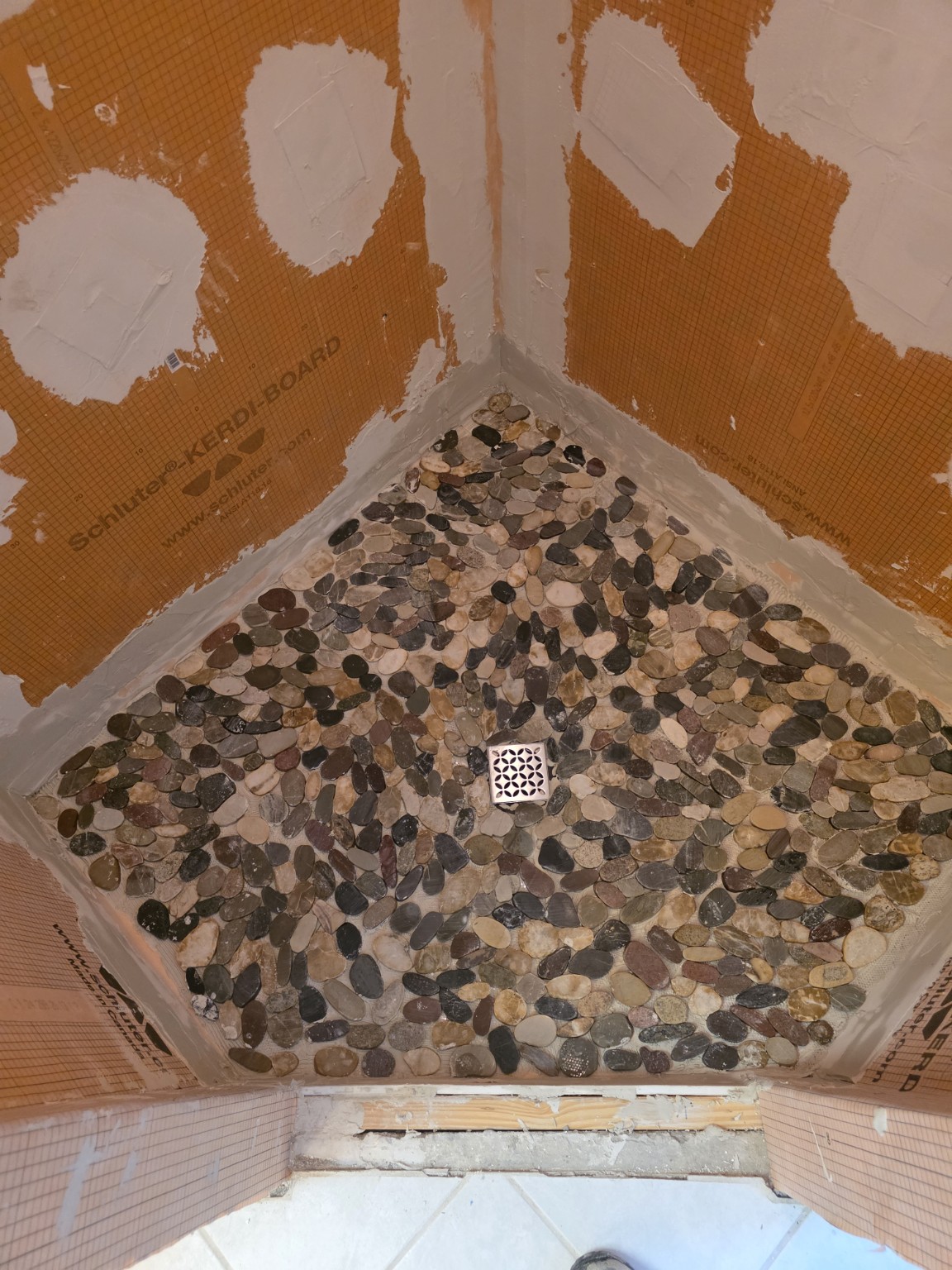 Pebble shower floor installation with wall boards still exposed