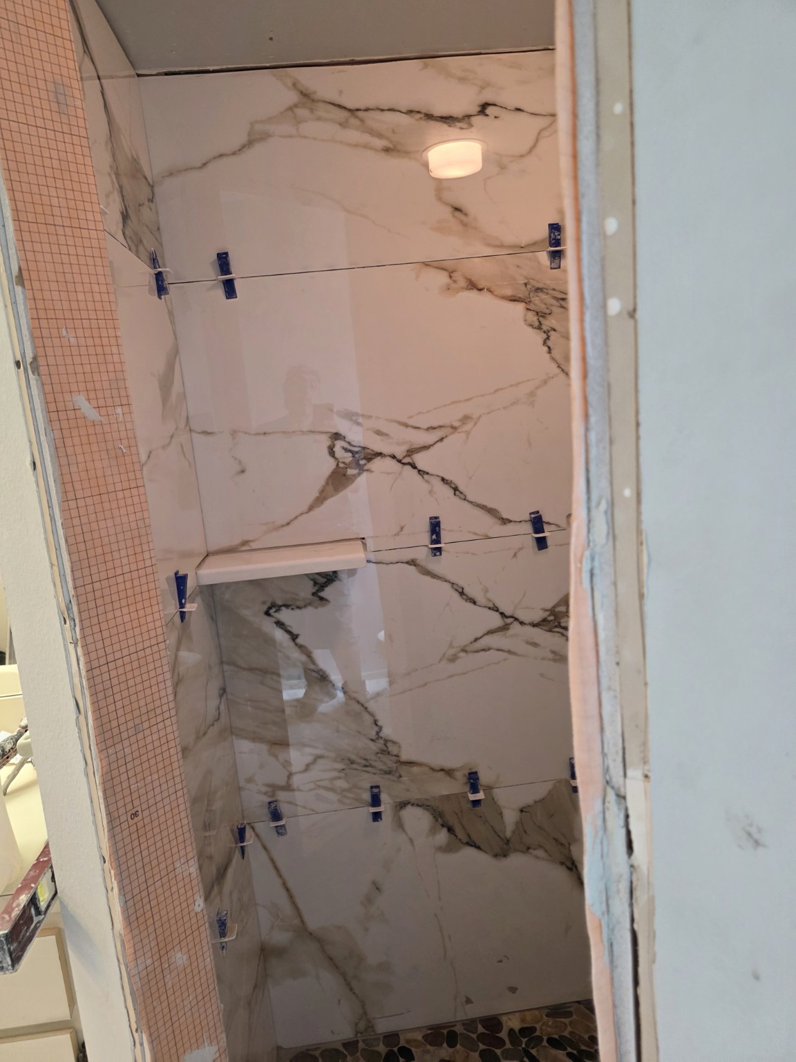 Marble-pattern shower wall tile installation with tile leveling clips still in place